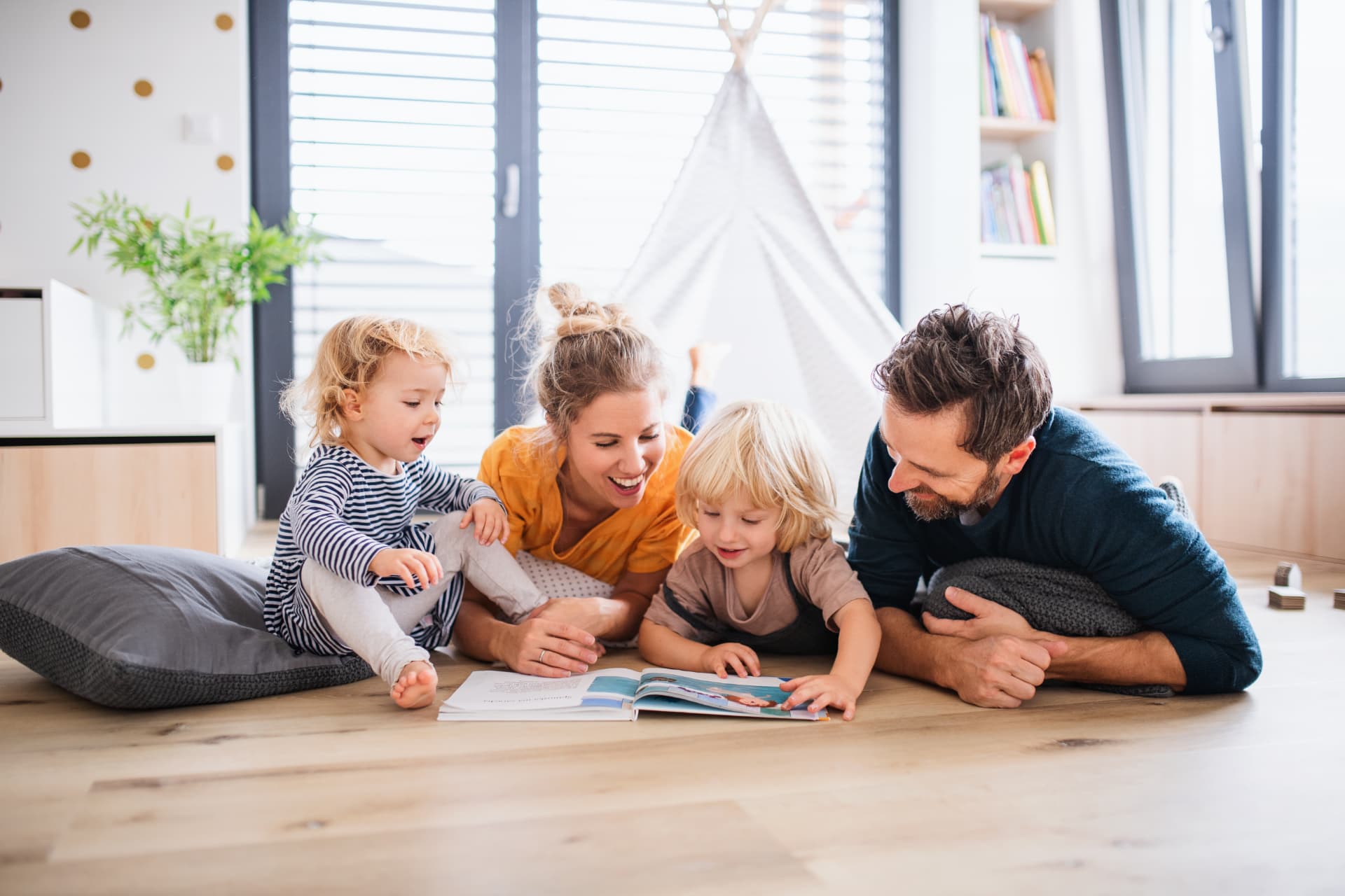 Familie mit zwei Kindern liest gemeinsam in einer hellen Wohnung